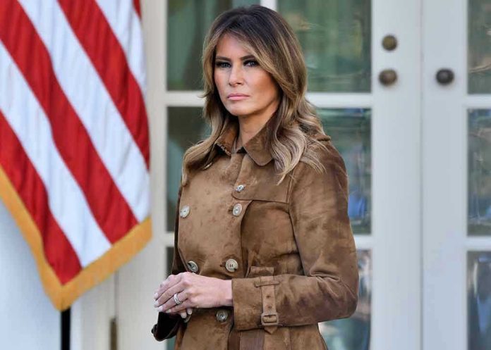 1572261598 Woman in brown coat beside American flag.