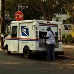 USPS mail carrier at truck near stop sign.