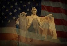 Statue of Abraham Lincoln seated against a backdrop of the American flag