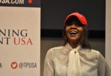 Candace Owens, Erika Kirk Feud ERUPTS – Private Meeting Held A woman wearing a red cap and a white blouse speaking at a political event