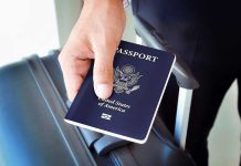 A person holding a United States passport next to a suitcase