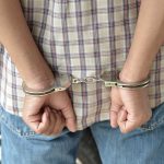 Beloved Child Star ARRESTED AGAIN – Troubling Downfall A person in handcuffs viewed from behind, wearing a plaid shirt and denim jeans