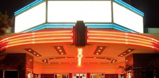 Entrance of a vintage movie theater illuminated by neon lights at night