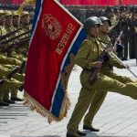 Soldiers marching with rifles and a red flag