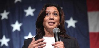 Woman speaking with microphone, American flag background.