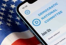 Massive DNC Money Laundering Fraud EXPLODES – See Report! Phone displaying Democratic National Committee website over flag.