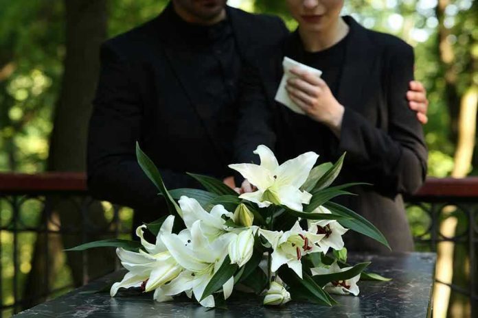 2314885229 Mourners in black holding white flowers at funeral.