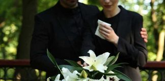 Mourners in black holding white flowers at funeral.