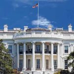U.S Citizens TRAPPED In Conflict – Beg Trump For Help! The White House with the American flag flying against a blue sky
