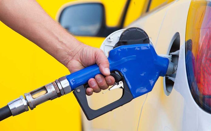 A person refueling a car at a gas station with a blue nozzle