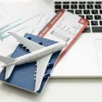 Flight Tickets SKYROCKET, Travelers Are Outraged! A model airplane on a blue passport next to a laptop and boarding pass