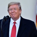 Trump Promises Mass Pardons to Staff Before Terms Up Man in suit and tie speaking at podium.