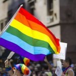 LGBTQ Americans Seeking Asylum – DENIED! People holding and waving a rainbow flag.