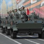 Tanks with military personnel in street parade formation.