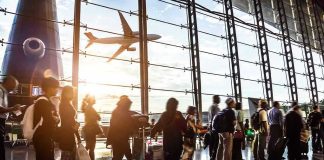 U.S. Secretly Sent Deportees to African Hotel — With Your Money Crowd of travelers in airport terminal with airplane outside.