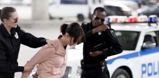 Police officers detain a woman beside a patrol car