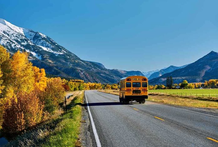 shutterstock_1151523266-2 A yellow school bus driving on a rural road surrounded by autumn trees and mountains