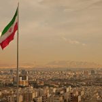 Trump Calls Iran Deal “Worst Ever,” Rejects Peace Iranian flag waving over a city skyline with mountains in the background