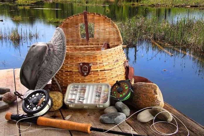 shutterstock_54257521 Fishing gear including a hat, basket, and fishing rods arranged by a serene water body