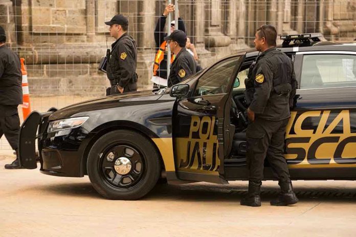 1493728583 Police officers standing and sitting near a patrol car.