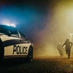 Police car with sirens next to running officers
