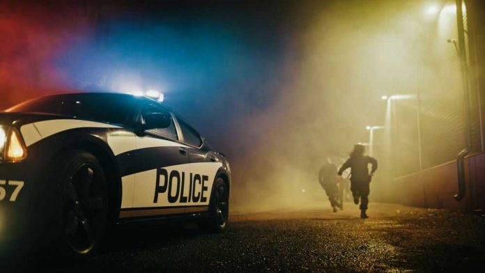 2232055249 Police car with sirens next to running officers