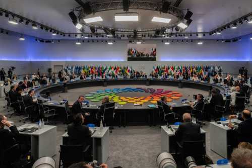 shutterstock_1369414589 A large round table meeting with global leaders and flags in the background