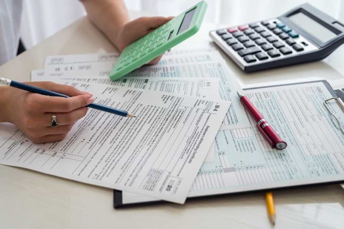 shutterstock_2048368346 Person calculating financial figures with documents and a calculator