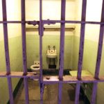 Interior of a prison cell with a toilet, sink, and metal bars