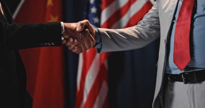 shutterstock_2699860513 Two individuals shaking hands in front of flags