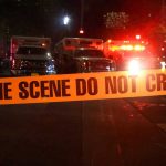 Crime scene tape with emergency vehicles in background.