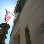 Guard Gunned Down Near White House — Now What? American flag at Department of Justice building exterior.