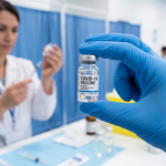 Gloved hand holding a COVID-19 vaccine vial in a clinic