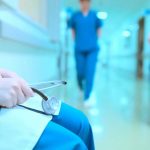 A healthcare professional holding a stethoscope in a hospital corridor