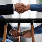 California’s One-Time Hit—Who Runs? Two people shake hands while exchanging cash under a table