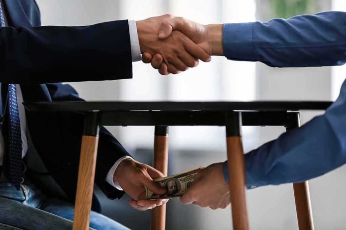 Two people shake hands while exchanging cash under a table
