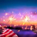 Hands holding sparklers with American flag background.