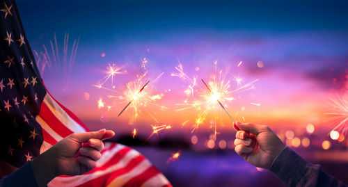 shutterstock_1706779105 Hands holding sparklers with American flag background.