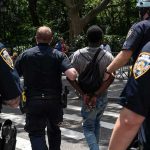 Bystanders Down — Cops Hunt Third Shooter Police escort a handcuffed man across a city street