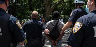Bystanders Down — Cops Hunt Third Shooter Police escort a handcuffed man across a city street