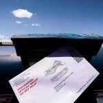 Voter Lists Or No Delivery — Seriously? Mail-in ballot being inserted into a blue USPS mailbox