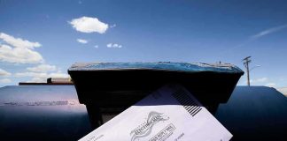 Voter Lists Or No Delivery — Seriously? Mail-in ballot being inserted into a blue USPS mailbox