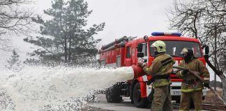 Firefighters spraying foam from a hose near a fire engine