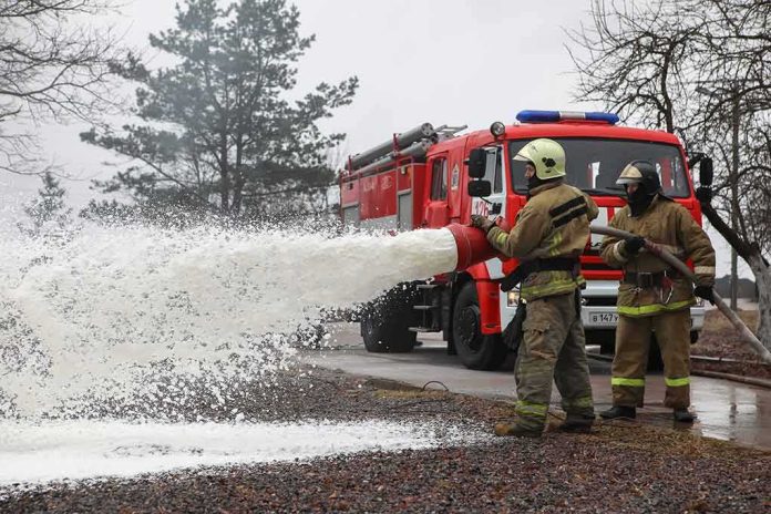 shutterstock_1721243686 Firefighters spraying foam from a hose near a fire engine