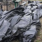 Burials Without Names Begin Black plastic bags piled outdoors near metal fencing