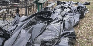 Black plastic bags piled outdoors near metal fencing