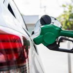 Green fuel nozzle pumping gas into a white car