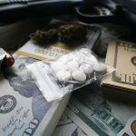 Military Crews Are Searching For Marijuana From Above Pills in a plastic bag on stacks of U.S. dollars with a handgun nearby