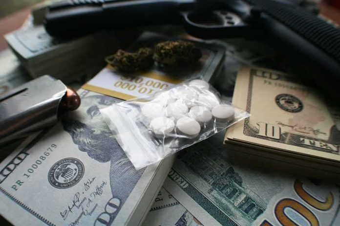 Pills in a plastic bag on stacks of U.S. dollars with a handgun nearby