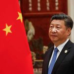 Beijing Blesses Kim’s Bomb Gambit Xi Jinping standing beside a Chinese flag